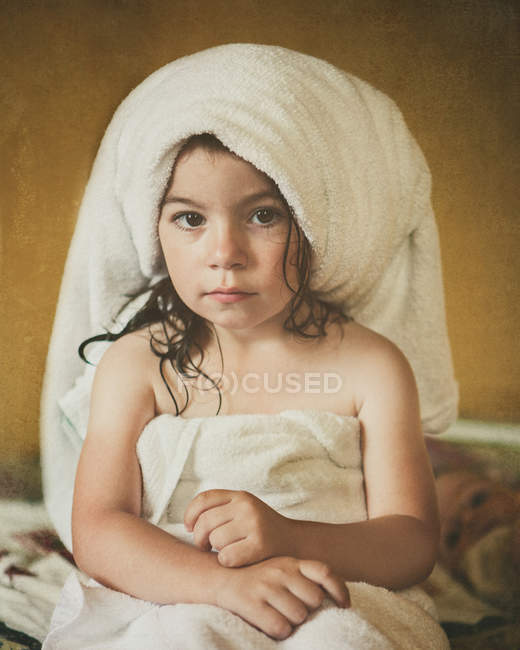 Porträt eines Mädchens, das nach dem Bad in Handtücher gehüllt auf dem Bett sitzt — Stockfoto