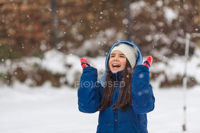 Menina feliz com as mãos no ar jogando na neve — Fotografia de Stock
