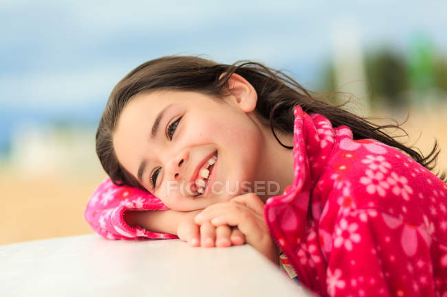 Chica sonriente apoyada en el borde de una mesa en la playa - foto de stock