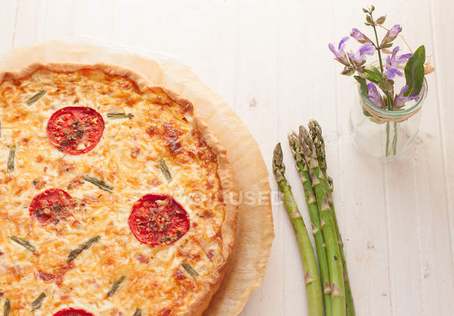Asparagus quiche on a table with asparagus and a jar of flowers — Stock Photo