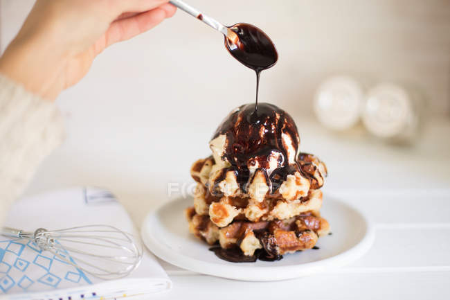 Mão humana derramando pilha de waffles com sorvete e molho de chocolate quente — Fotografia de Stock