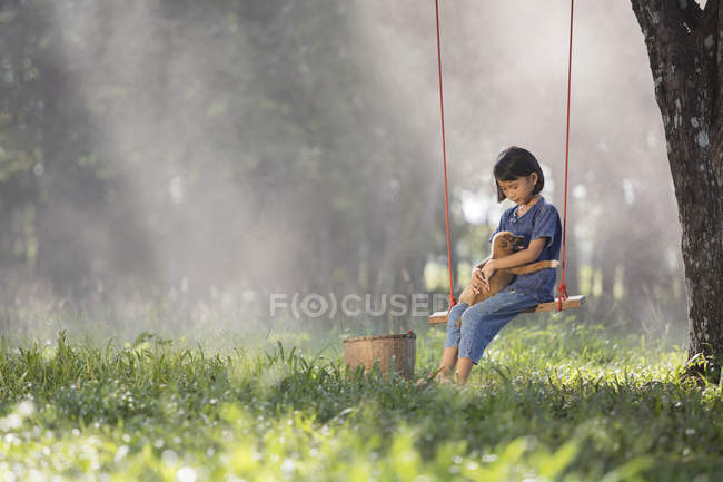 Menina sentada em um balanço com o cão no colo — Fotografia de Stock