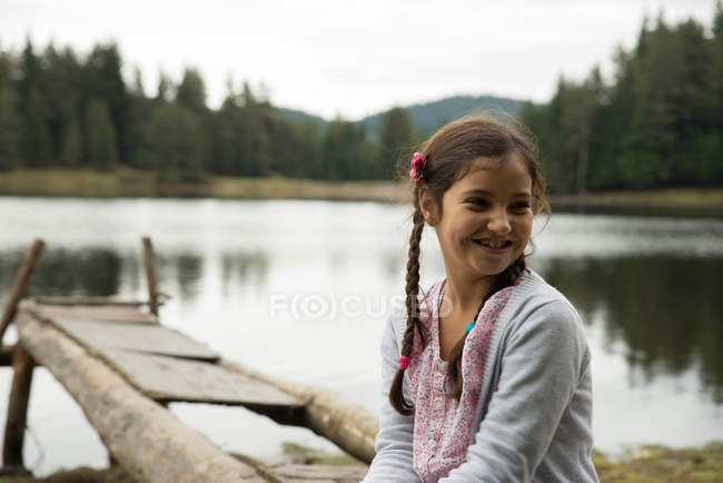 Sorridente ragazza seduta al lago e guardando lateralmente — Foto stock