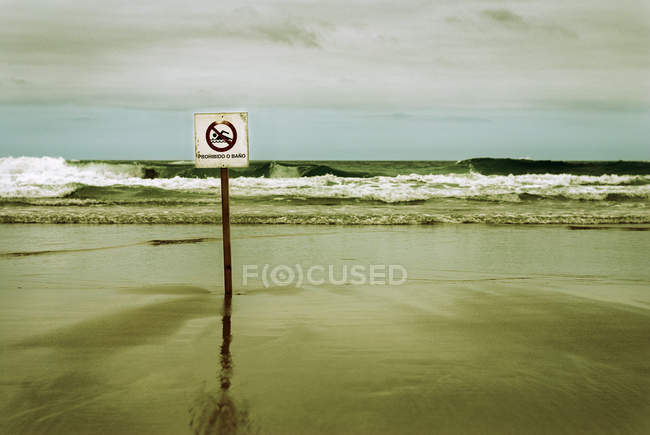 Praia deserta com sinal proibindo a natação — Fotografia de Stock