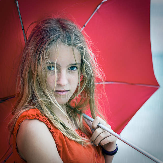 Porträt eines ernsten Mädchens mit rotem Regenschirm, das in die Kamera blickt — Stockfoto