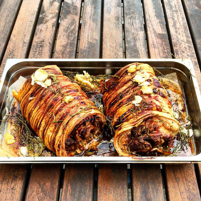 Tasty roasted porchetta in baking tray over wooden table — Stock Photo