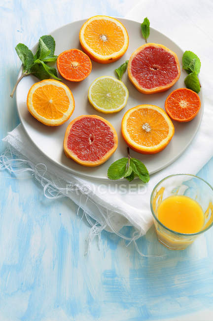 Slices of citrus fruits on plate and glass of juice — Stock Photo