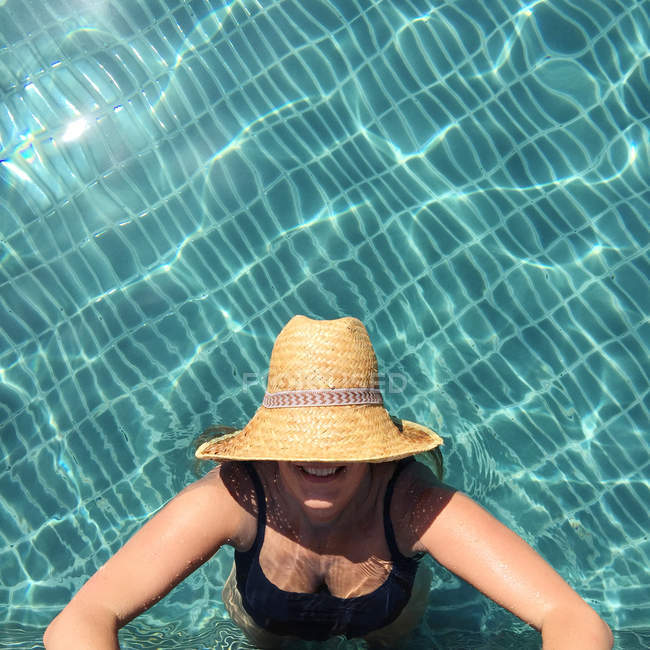 Mulher usando chapéu de palha em pé na piscina e olhando para cima — Fotografia de Stock
