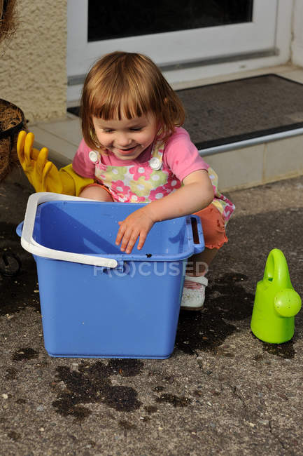 Chica agachada junto a un cubo listo para limpiar - foto de stock