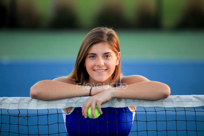 Portrait d'adolescente souriante penchée sur le filet du court de tennis — Photo de stock