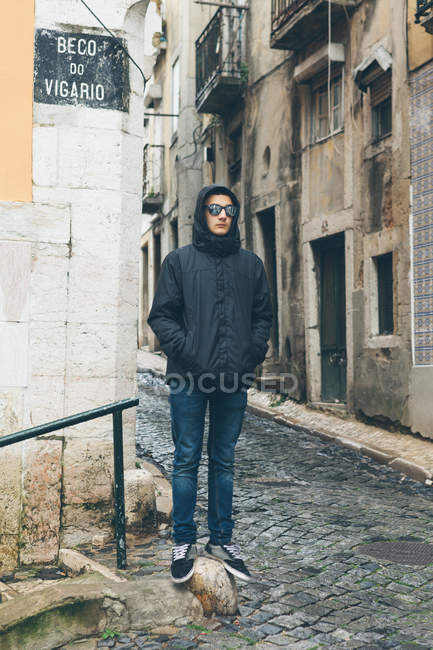 Teenage Boy indossa giacca con cappuccio e occhiali da sole in piedi sulla strada, Alfama, Lisbona, Portogallo — Foto stock
