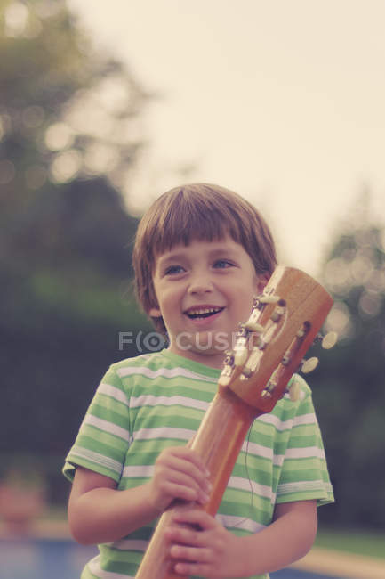 Усміхнений хлопчик тримає гітару на відкритому повітрі — стокове фото