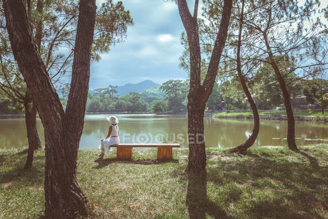 Rückansicht einer Frau, die auf einer Bank in der Nähe des Sees sitzt, Farbton, Vietnam — Stockfoto