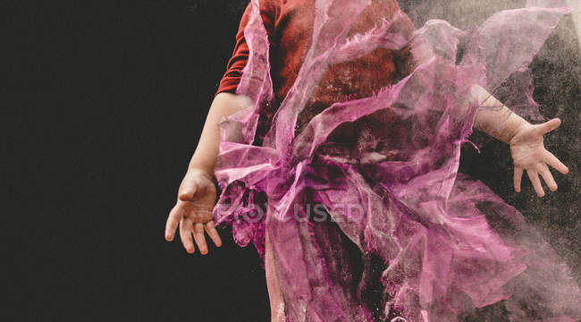 Sección media de una chica en una falda de tul jugando en el polvo contra el fondo negro - foto de stock