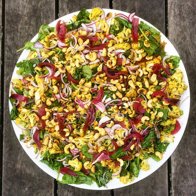 Салат из цветной капусты с орехами кешью на белой тарелке, вид сверху — стоковое фото
