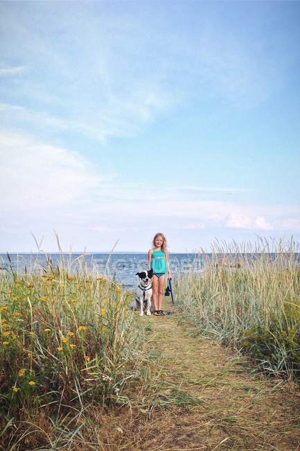 Rubia chica caminando en playa con perro - foto de stock