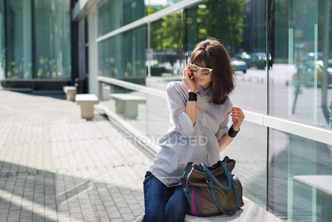 Girl talking on mobile phone and leaning on glass wall on street — Stock Photo