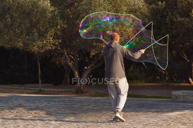 Mann steht im Park und macht große Seifenblase — Stockfoto