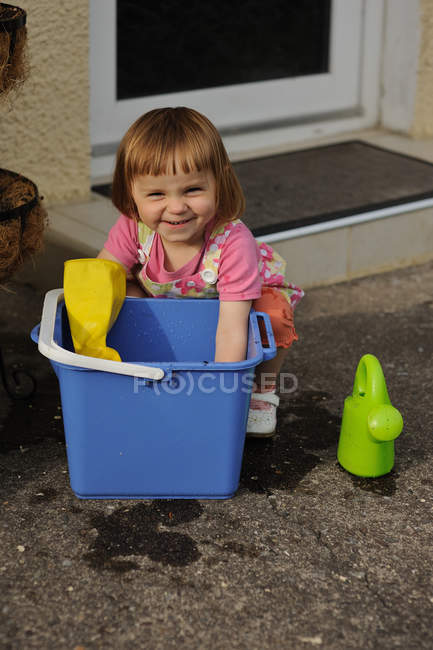 Smiling little Girl with hands in a bucket — Stock Photo