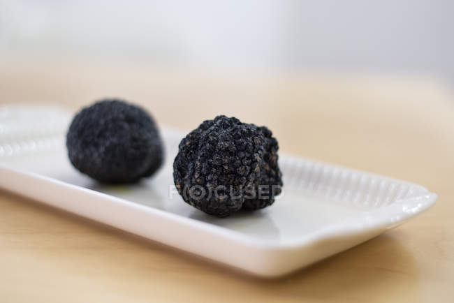 Nahaufnahme schwarzer Trüffel auf weißem Teller und Holztisch — Stockfoto