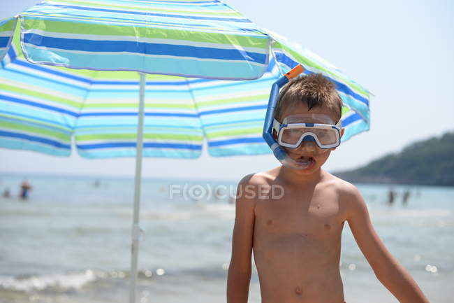 Мальчик в плавках и маске стоит на пляже — стоковое фото