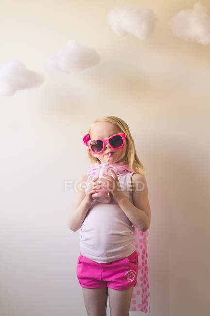 Mädchen in pinkfarbener Kleidung und Sonnenbrille trinkt einen rosa Milchshake — Stockfoto