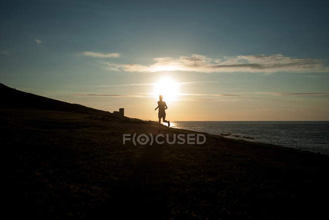 Silhueta de homem correndo na praia ao pôr do sol — Fotografia de Stock