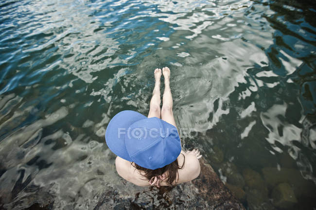 Woman wearing cap sitting at the edge of a lake — Stock Photo
