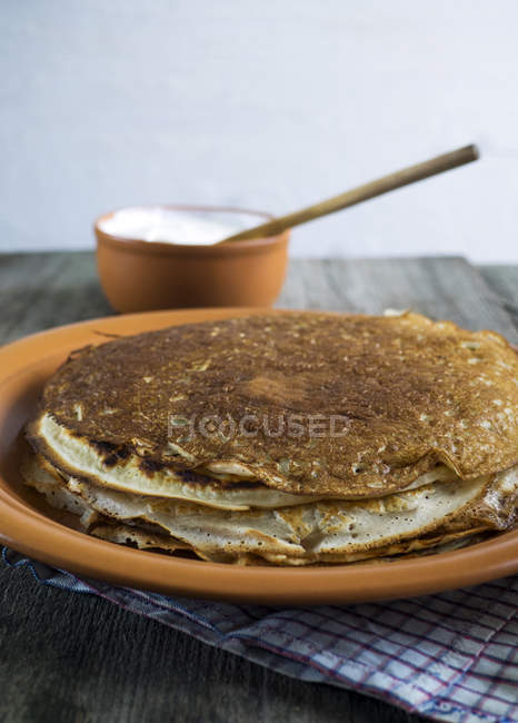Stack of crepe pancakes on plate with pot of cream — Stock Photo