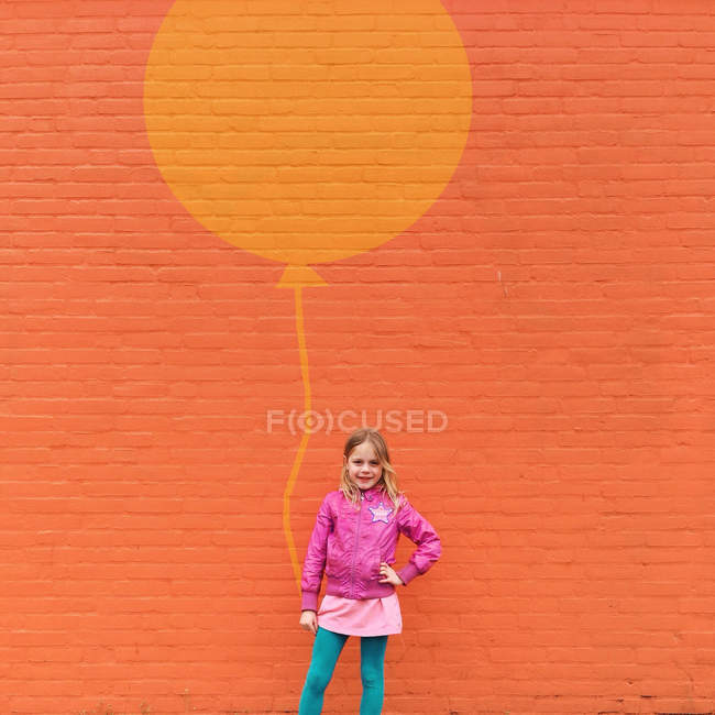 Mädchen steht mit Luftballon vor einer orangefarbenen Wand — Stockfoto