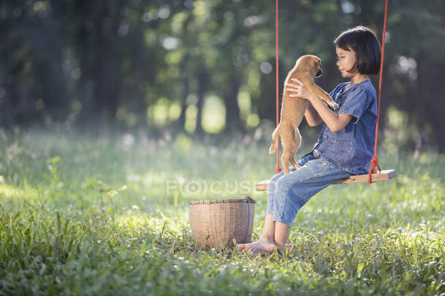 Girl sitting on rope swing with dog on lap — Stock Photo