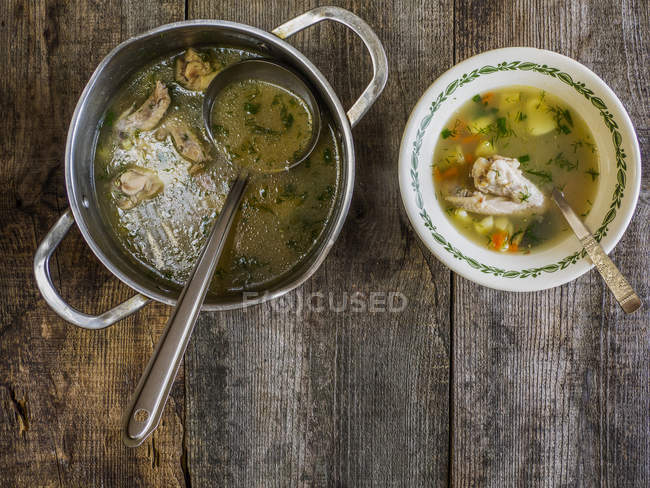 Saucepan and bowl of chicken soup on wooden table — Stock Photo