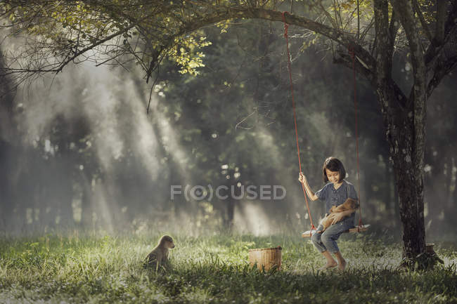 Девушка сидит на качелях с собакой на коленях — стоковое фото