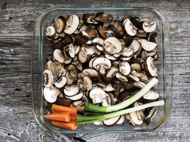 Dish with raw sliced mushrooms, carrots and spring onions on wood — Stock Photo
