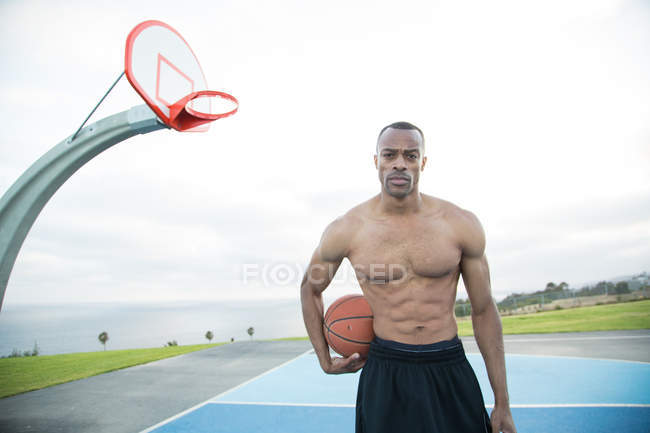 Retrato de un joven sosteniendo una pelota de baloncesto en un parque - foto de stock