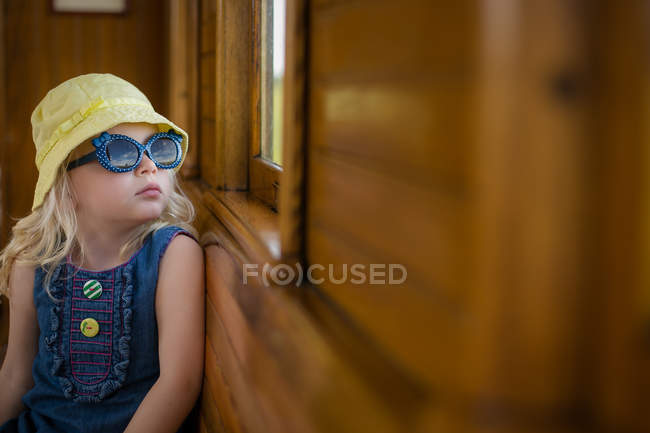 Mädchen mit Sommermütze und Sonnenbrille sitzt im Zug und schaut aus dem Fenster — Stockfoto
