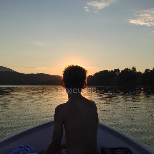 Rückansicht eines Jungen, der im Boot sitzt und den Sonnenuntergang beobachtet — Stockfoto