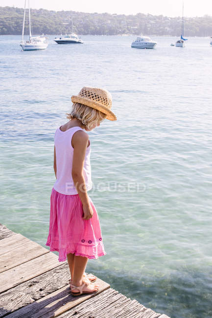 Ragazza in piedi su un molo e guardando in acqua di mare — Foto stock