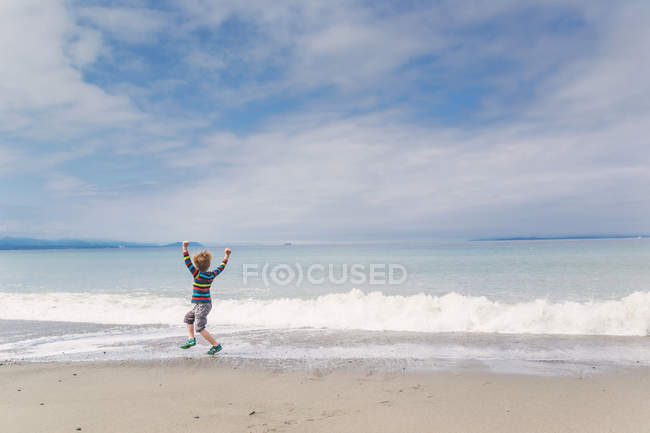 Вид сзади счастливого мальчика, играющего на пляже — стоковое фото