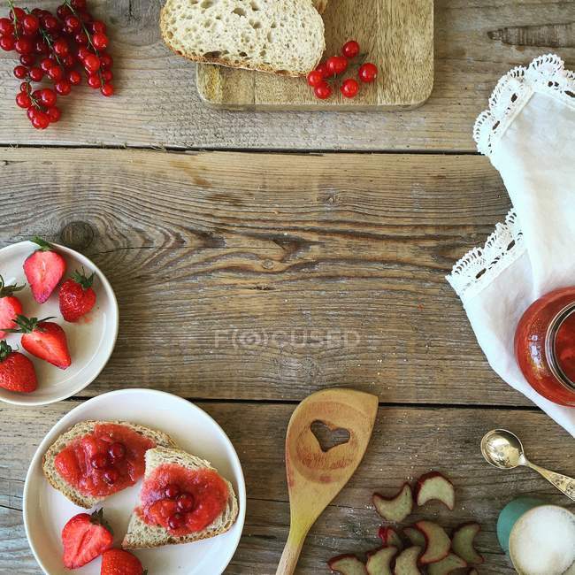 Strawberries, redcurrants, bread and jam on rustic wooden table — Stock Photo