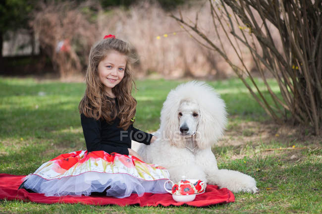 Портрет девушки, сидящей с белым пуделем на одеяле для пикника — стоковое фото