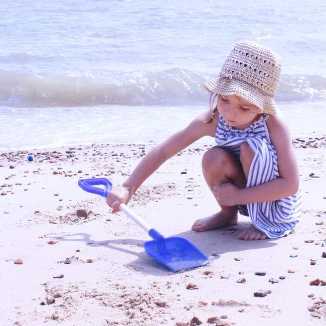 Дівчина в солом'яному капелюсі грає на пляжі з пластиковою лопатою — стокове фото