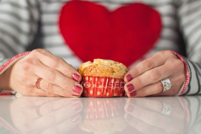 Cropped image of Woman with pink manicure, wearing top with big red heart, holding muffin — Stock Photo