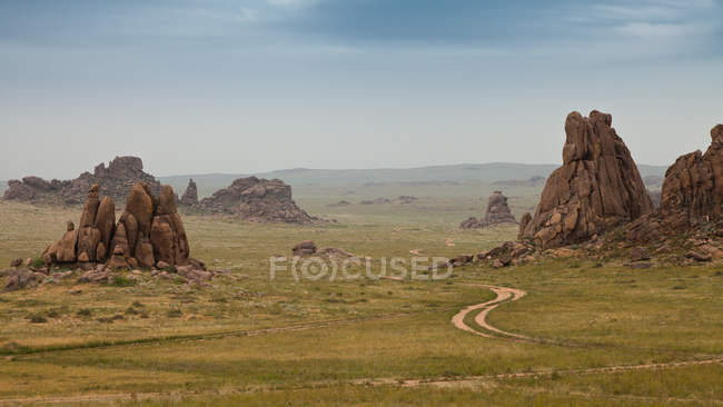 Грязная дорожка между скальными образованиями в поле — стоковое фото