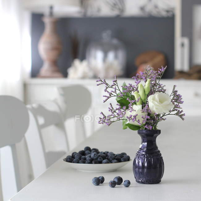 Fresh cut flowers in vase with fresh blueberries on dining table — Stock Photo