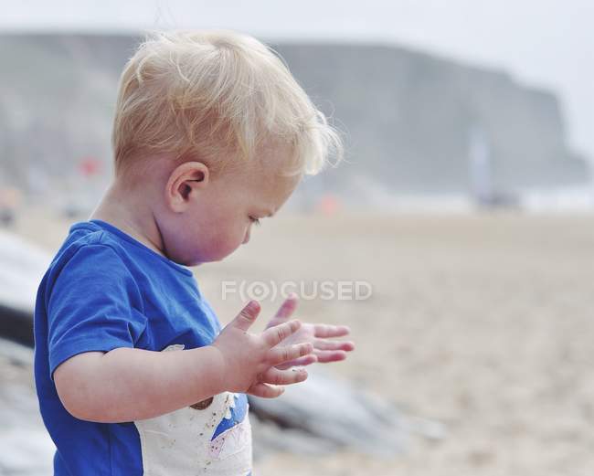 Блондин маленький мальчик смотрит на руки на песчаном пляже — стоковое фото