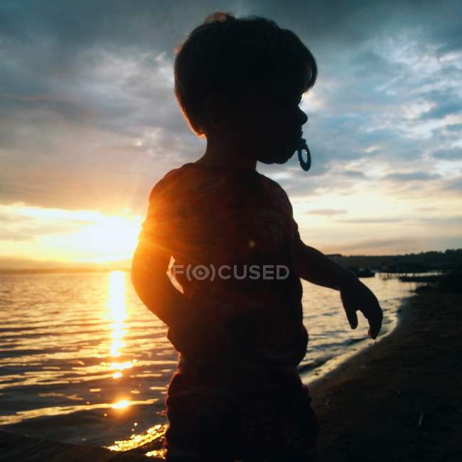 Silhouetted niño jugando en la playa al amanecer - foto de stock