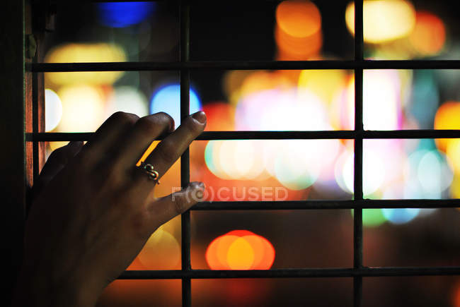 Primo piano della mano femminile su griglia metallica con illuminazione sullo sfondo — Foto stock