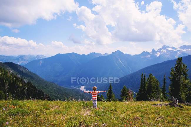 Маленький хлопчик стоїть з обіймами, витягнутими в природі і дивиться на гори — стокове фото