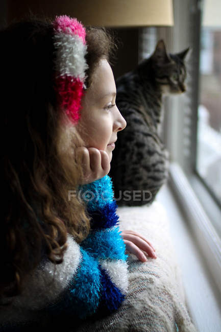 Vue latérale de belle fille avec chat tabby mignon regardant par la fenêtre — Photo de stock